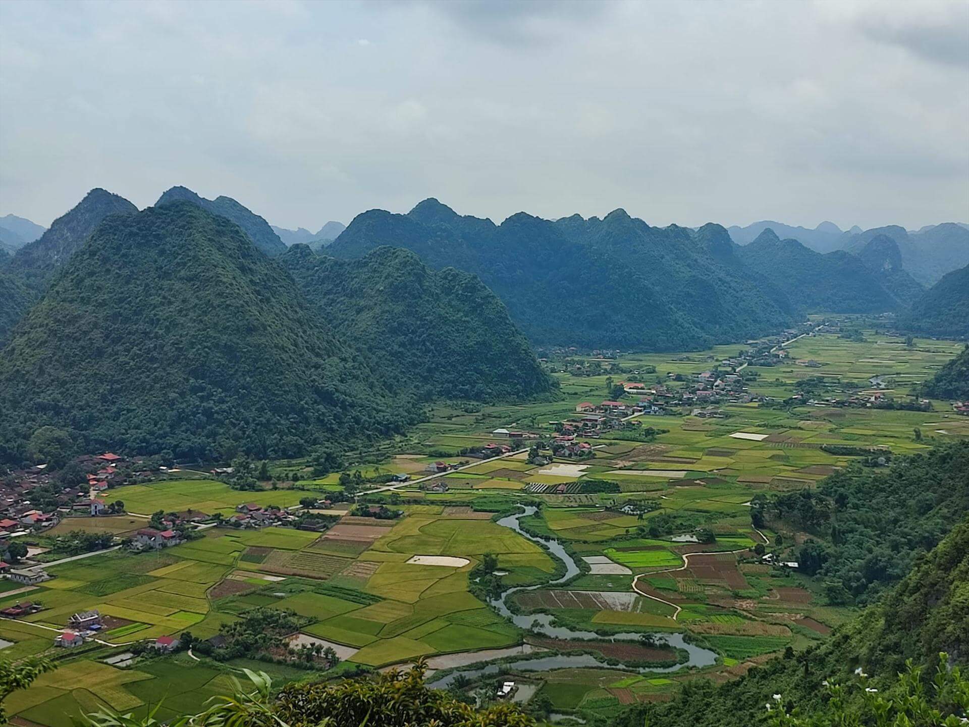 Dramatic limestone karst formations rising above green valleys and winding rivers in Vietnam.